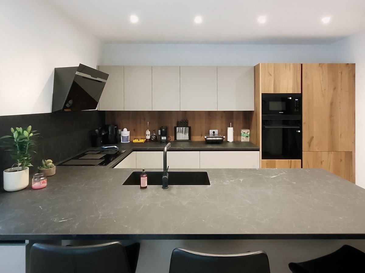 Cucina con penisola in pietra scura, sgabelli neri, colonne in rovere e forni a incasso neri